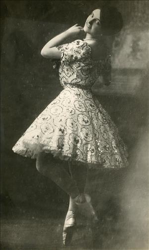 A young woman in a dress and toe shoes smiles back at the camera over her left shoulder. 